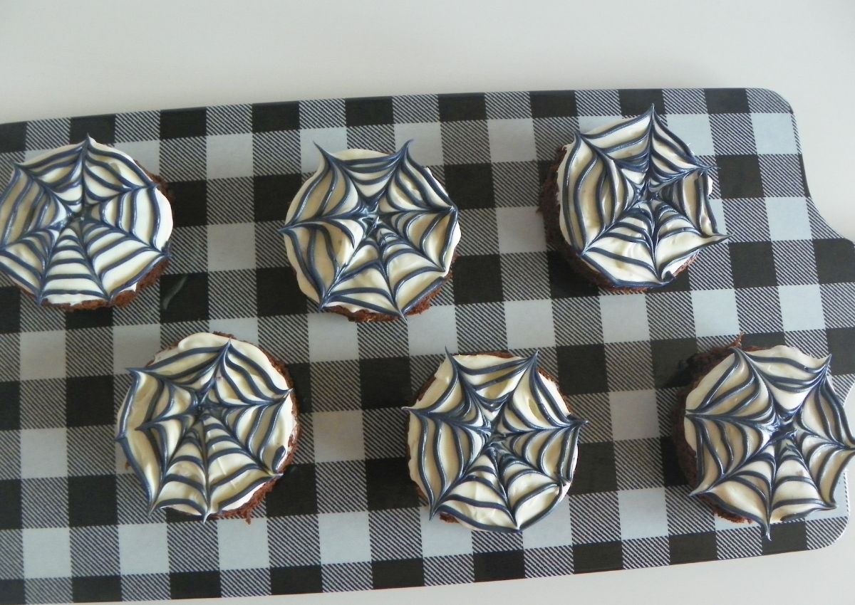 Six spider web brownie on a wooden cutting board.