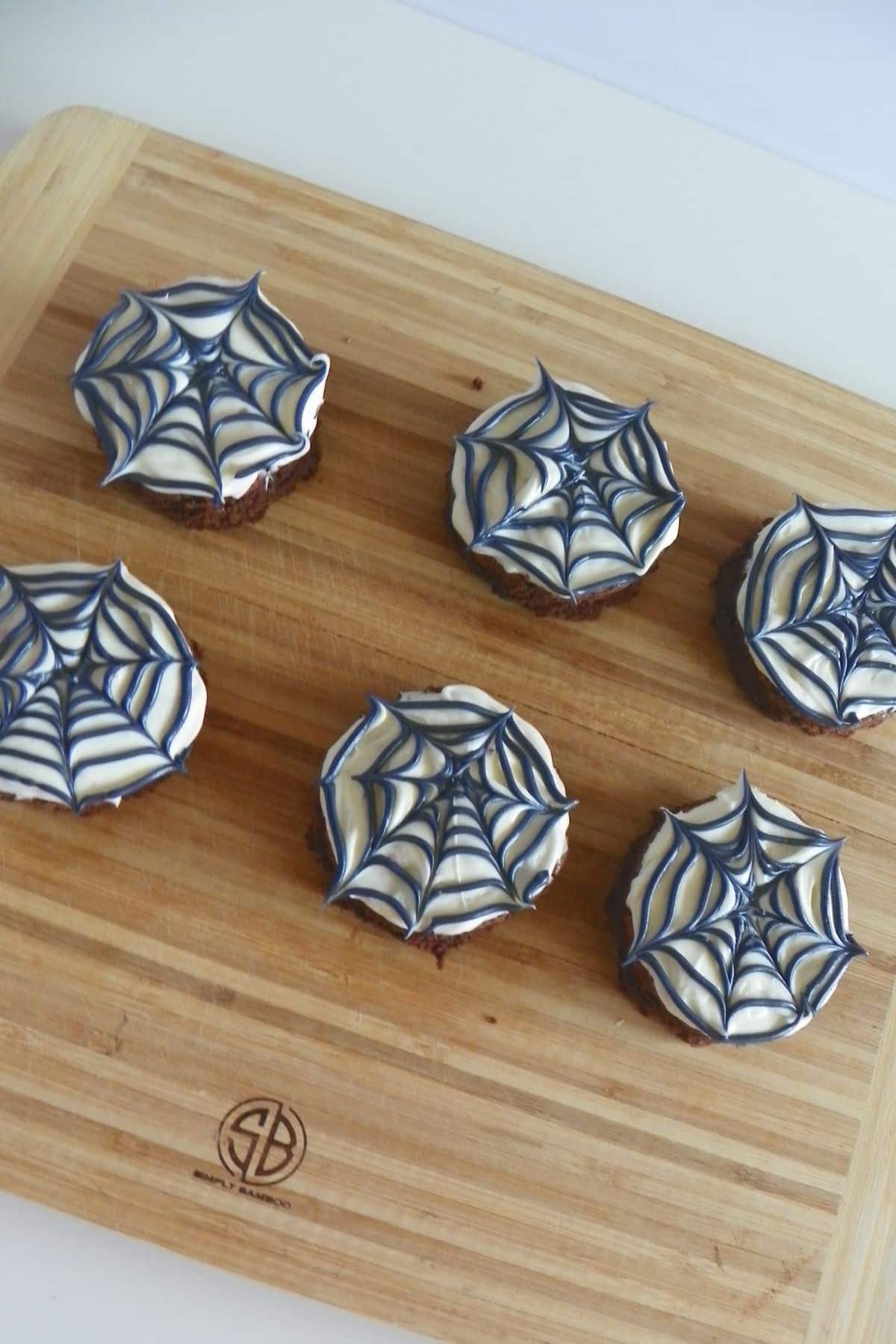 Six spider web brownie on a wooden cutting board.