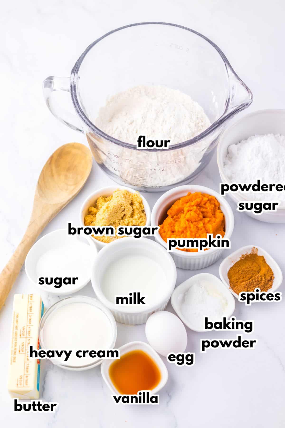Flour, brown sugar, pumpkin, powdered sugar, sugar, milk, heavy cream, egg, vanilla, baking powder, spices, and butter on a counter.