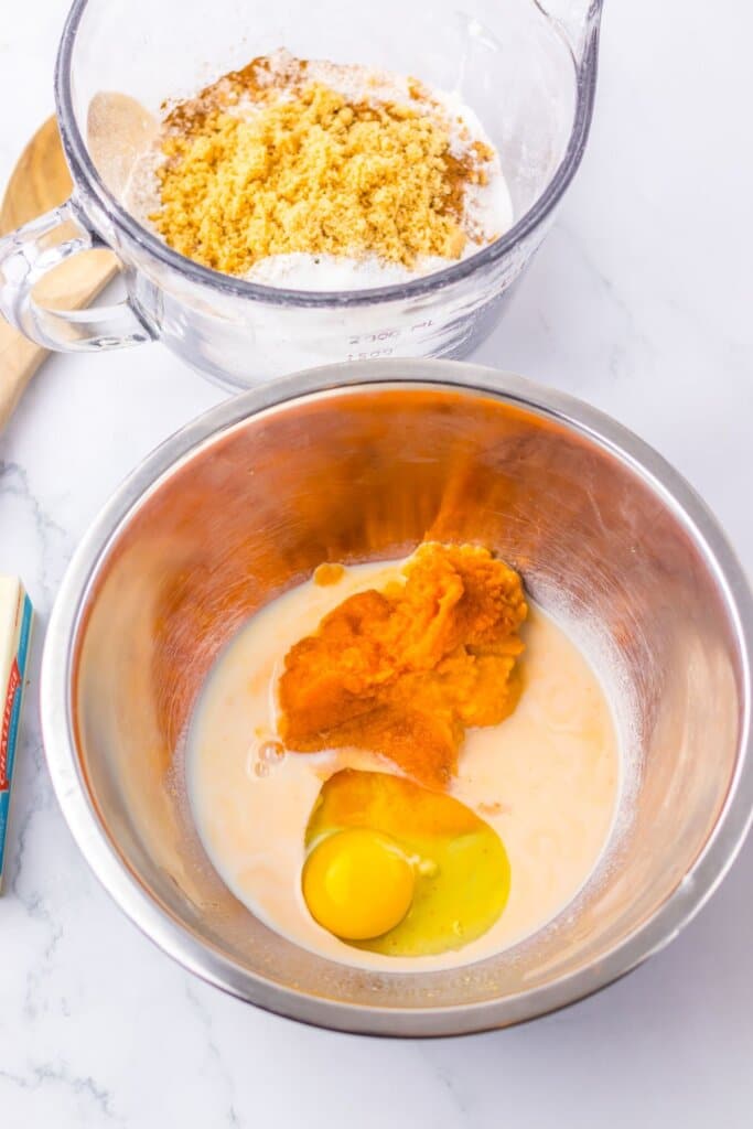 Eggs, pumpkin, and wet ingredients being mixed together in a stainless steel mixing bowl.
