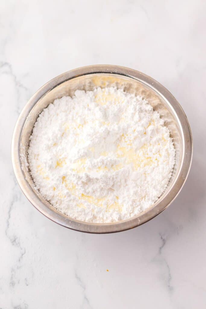 Powdered sugar and heavy cream being mixed together in a stainless steel mixing bowl.