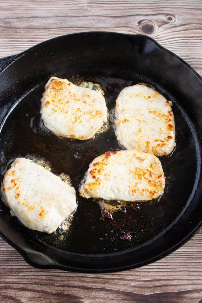 Pork chops being seared on both sides.