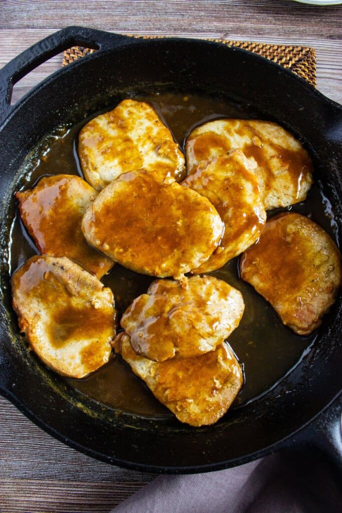 Pork chops being added back to a cat iron skillet.