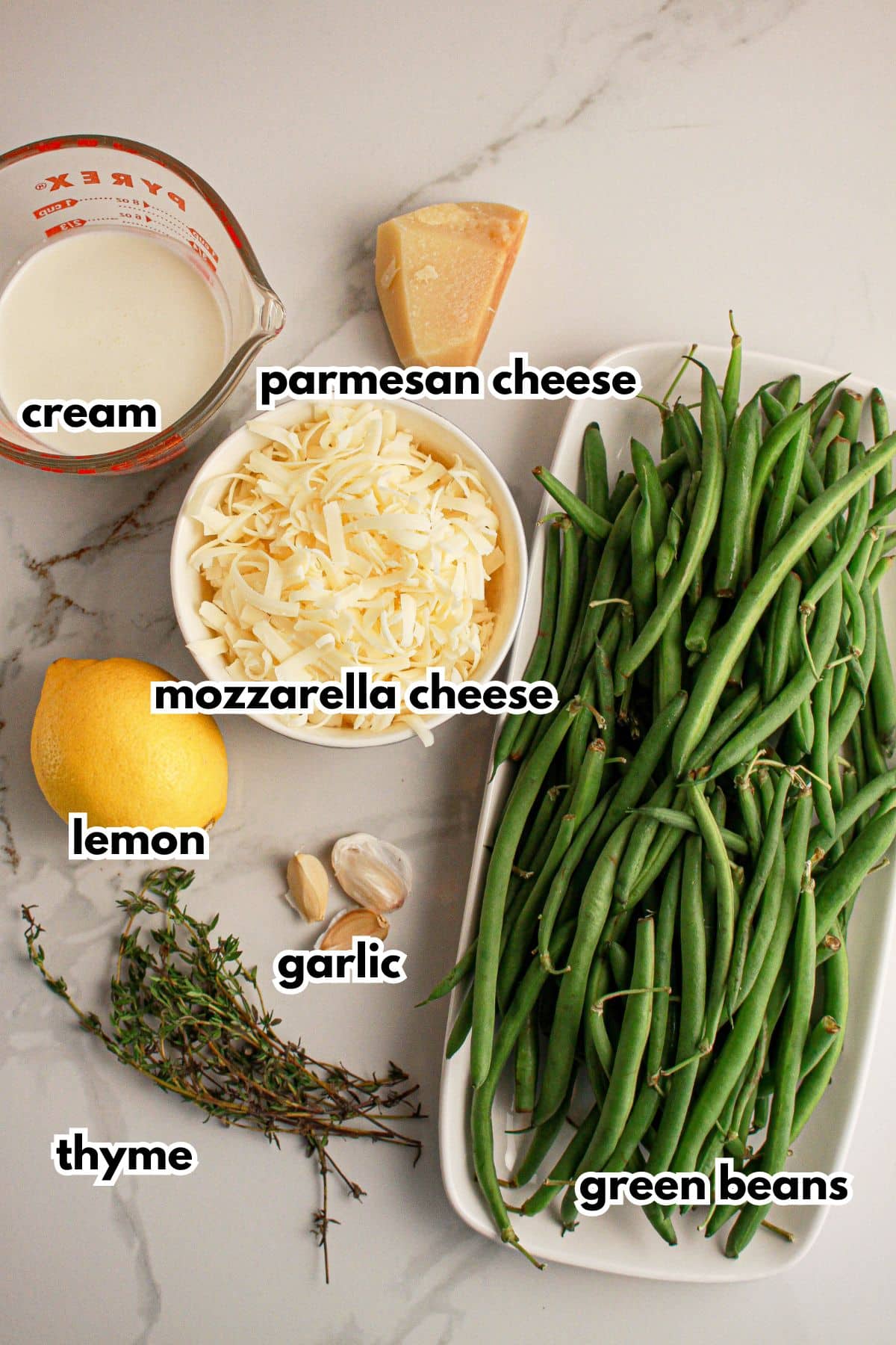 Cream, parmesan cheese, mozzarella cheese, lemon, garlic, thyme, and green bean on a counter.