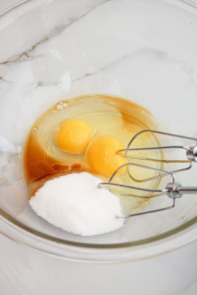 Eggs, vanilla, and sugar in a glass mixing bowl.