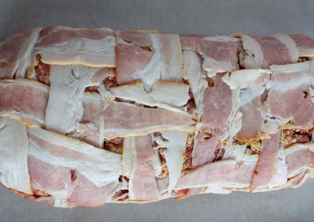 Bacon being wrapped around meatloaf.