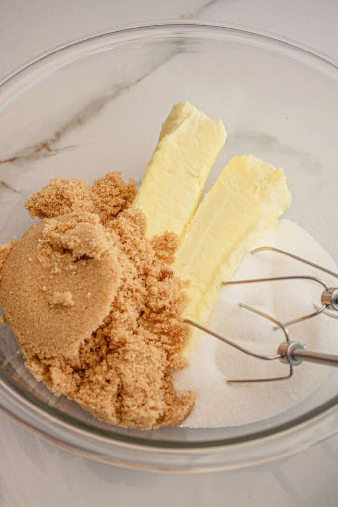 Butter, brown sugar, and sugar being mixed in a glass mixing bowl.