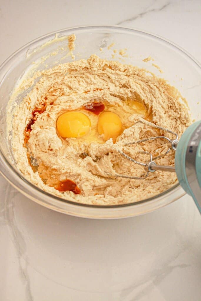 Eggs and vanilla being added to dough in a glass mixing bowl.