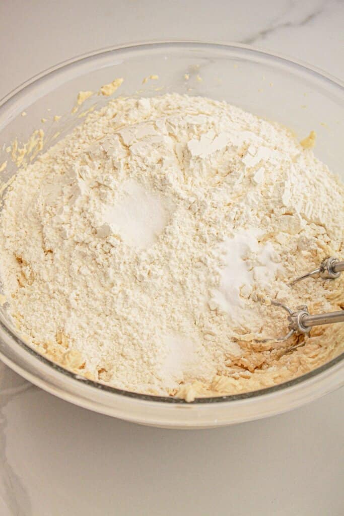 Dry ingreidents being added to dough in a glass mixing bowl.