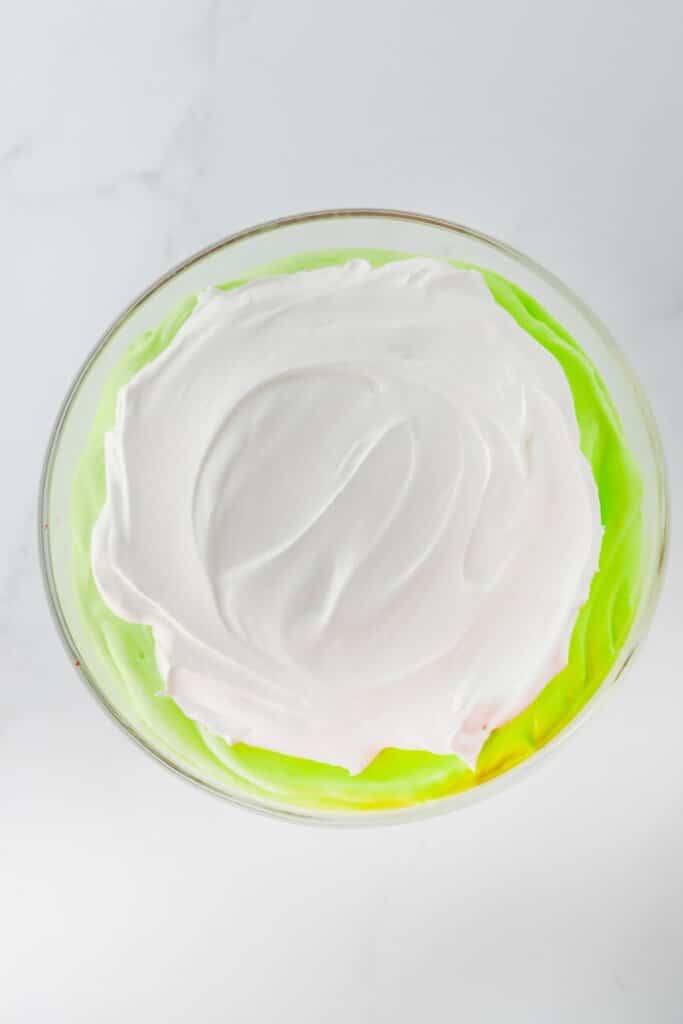 Cool Whip being spread on top of green pudding.