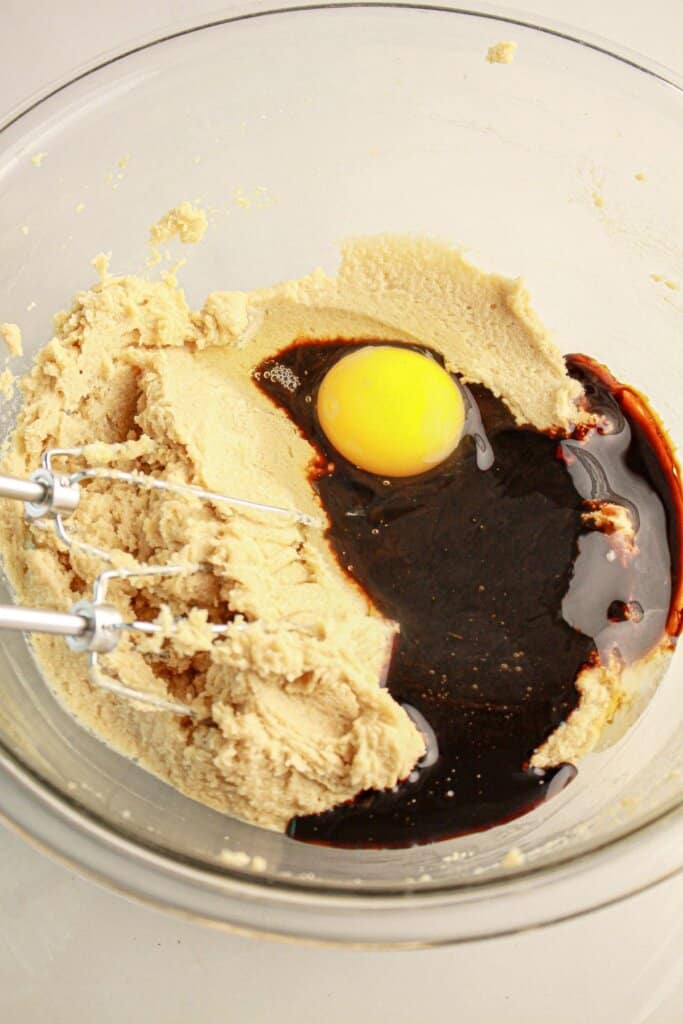 Egg being added to cookie dough in a bowl.