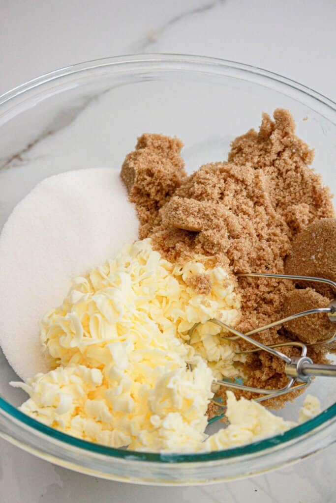 Butter, brown sugar and white sugar being mixed in a glass bowl.