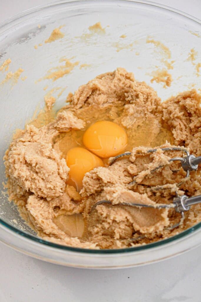 Eggs being added to butter and sugar in a glass bowl.