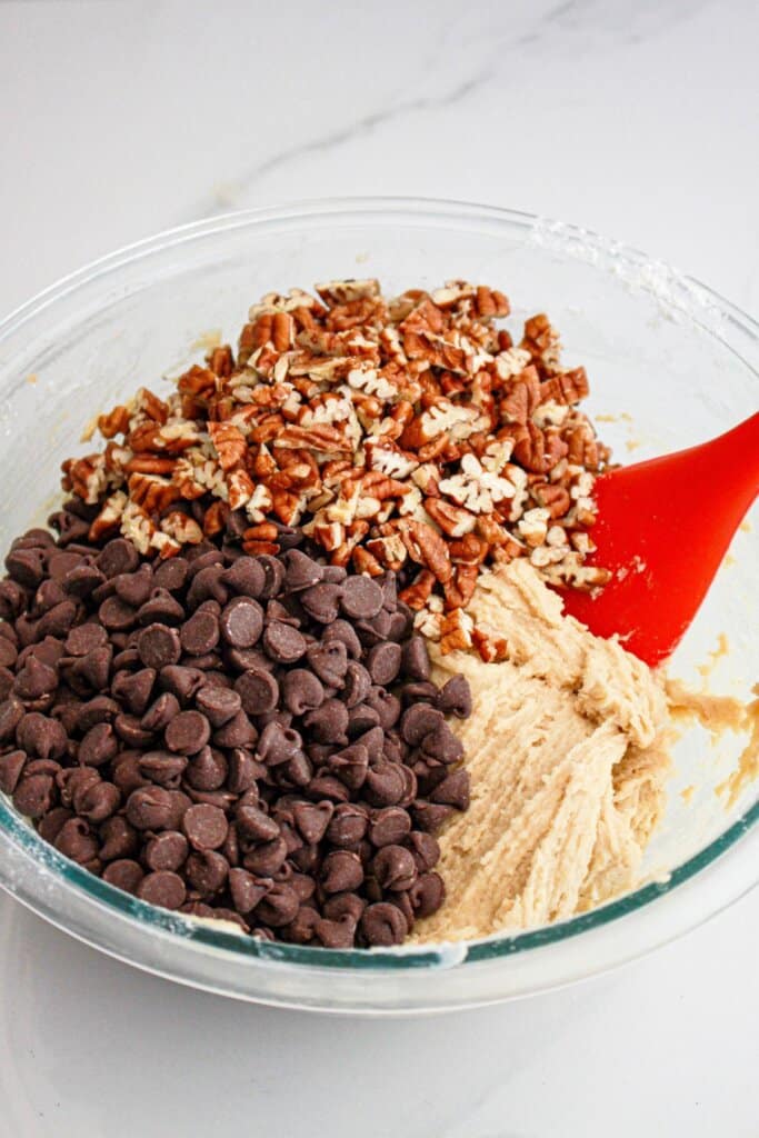 Dough, pecans, and chocolate chips in a mixing bowl.
