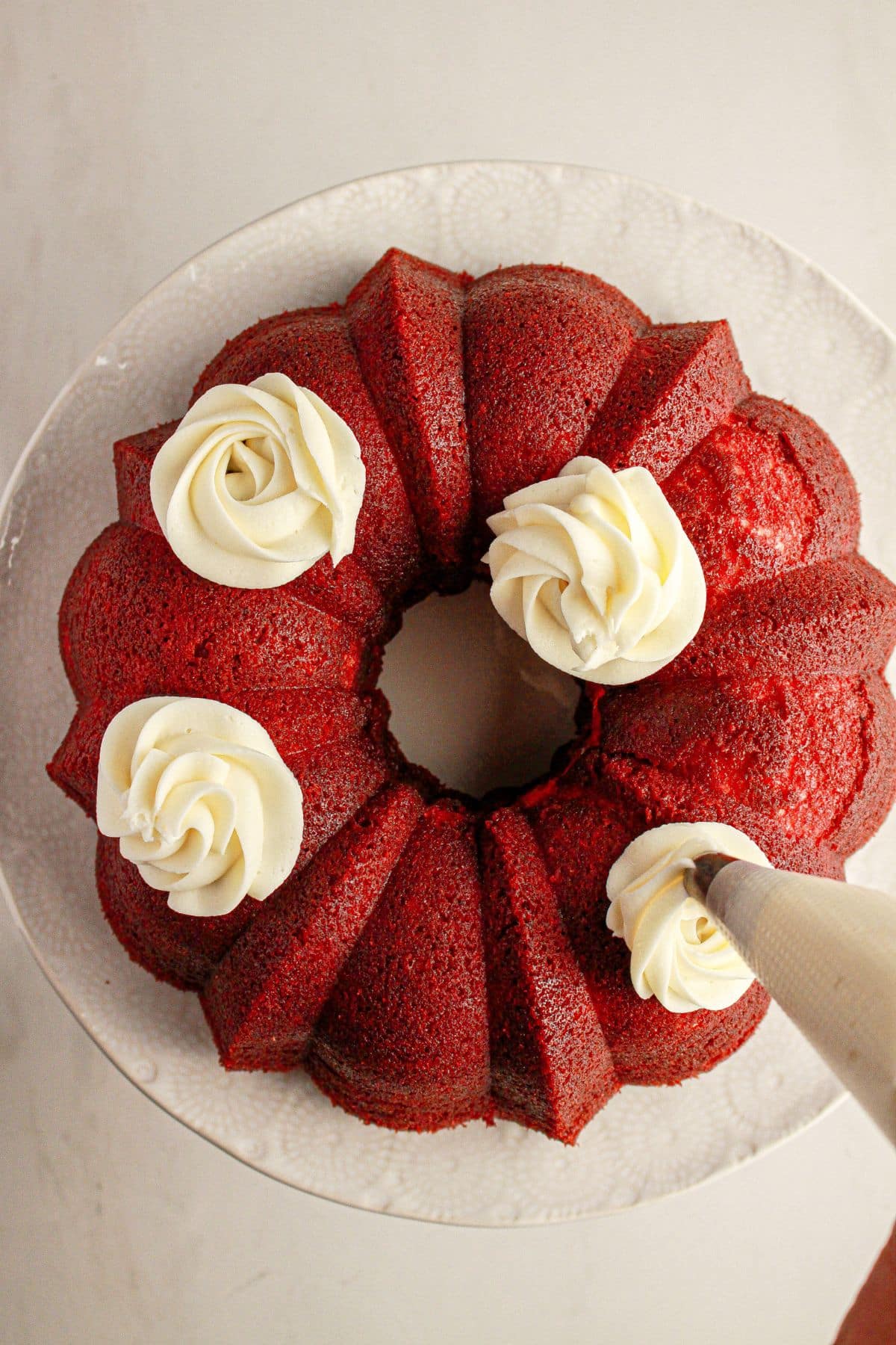 Cream cheese frosting being added on top of a bundt cake.