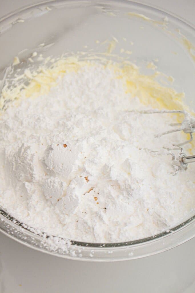 Powdered sugar being added to creamed butter.