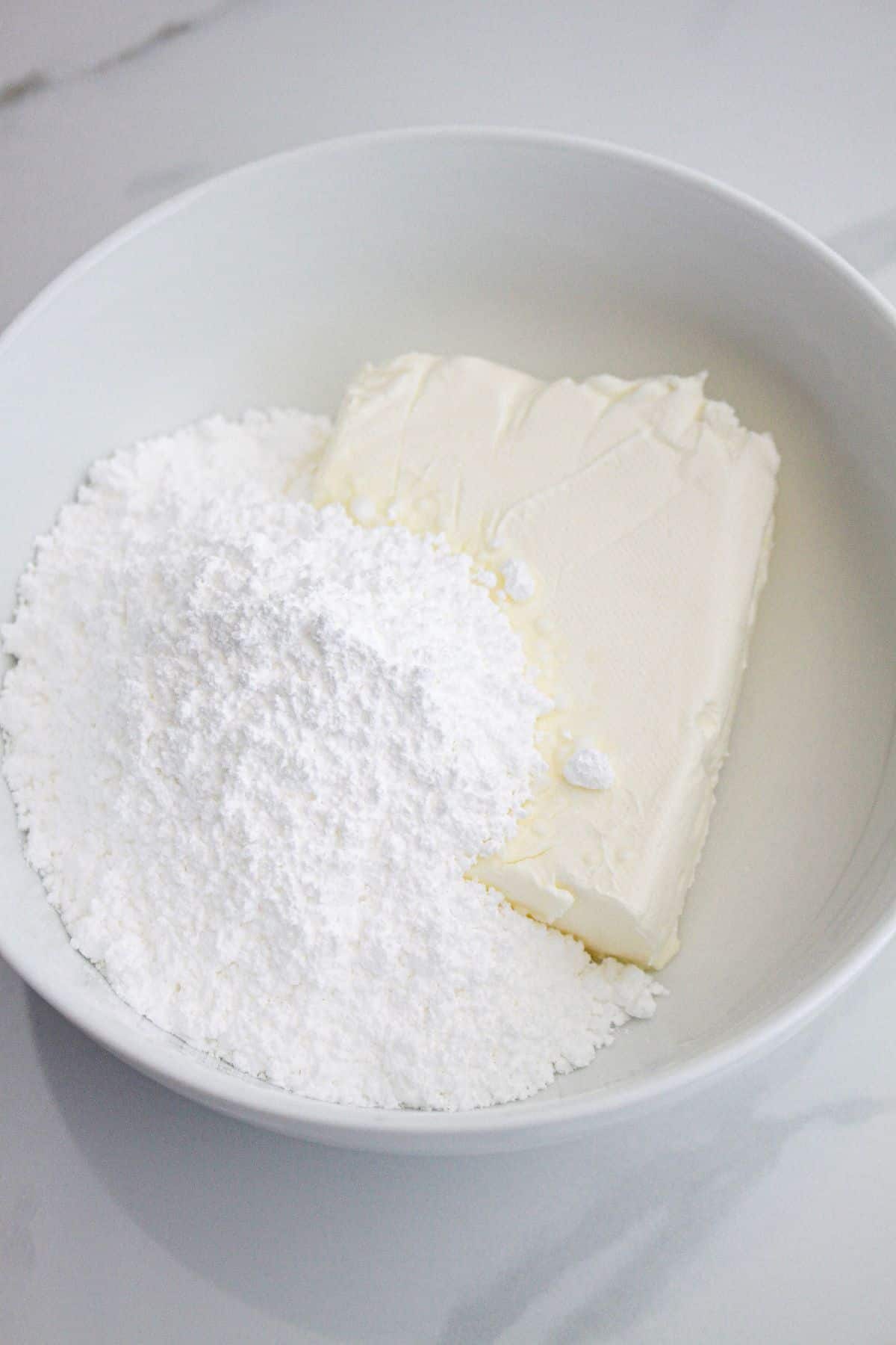 Cream cheese and powdered sugar being mixed in a bowl.