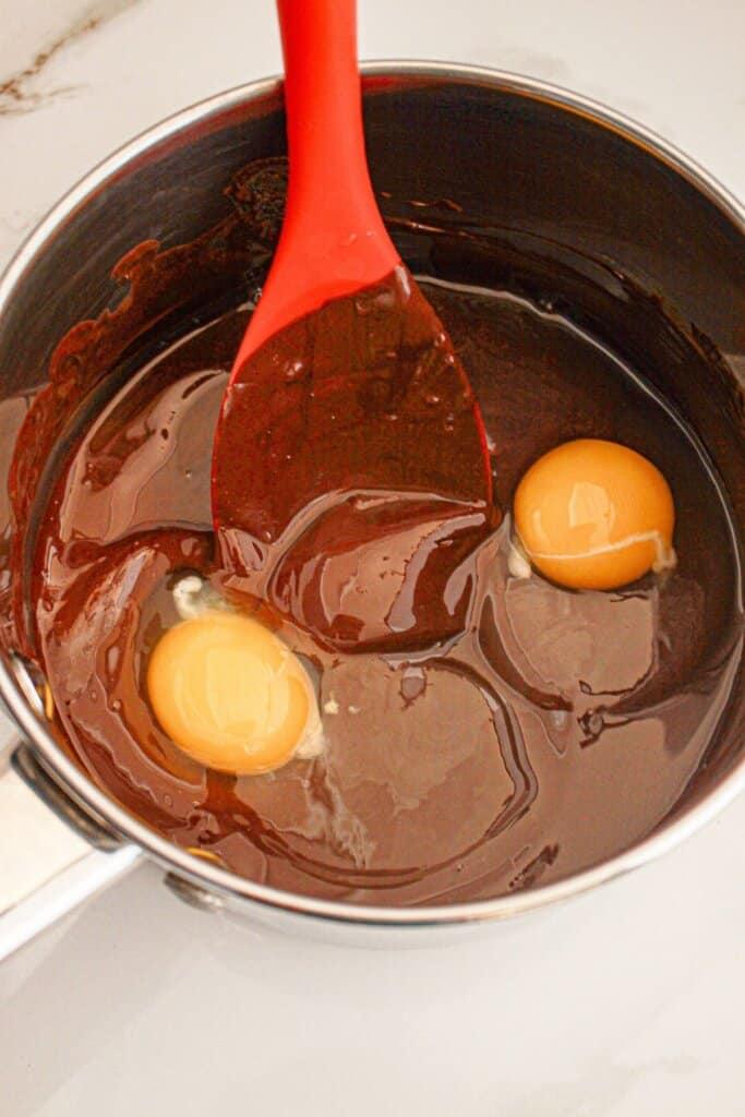 Eggs being added to melted chocolate in a saucepan.