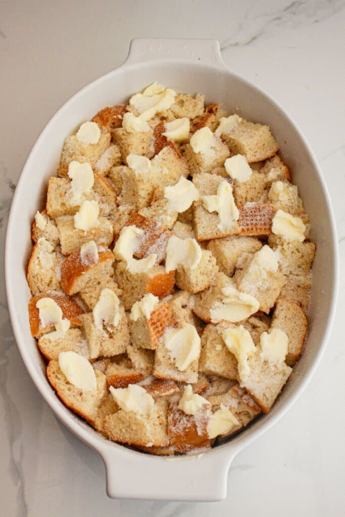 Butter on top of bread slices in a baking dish.