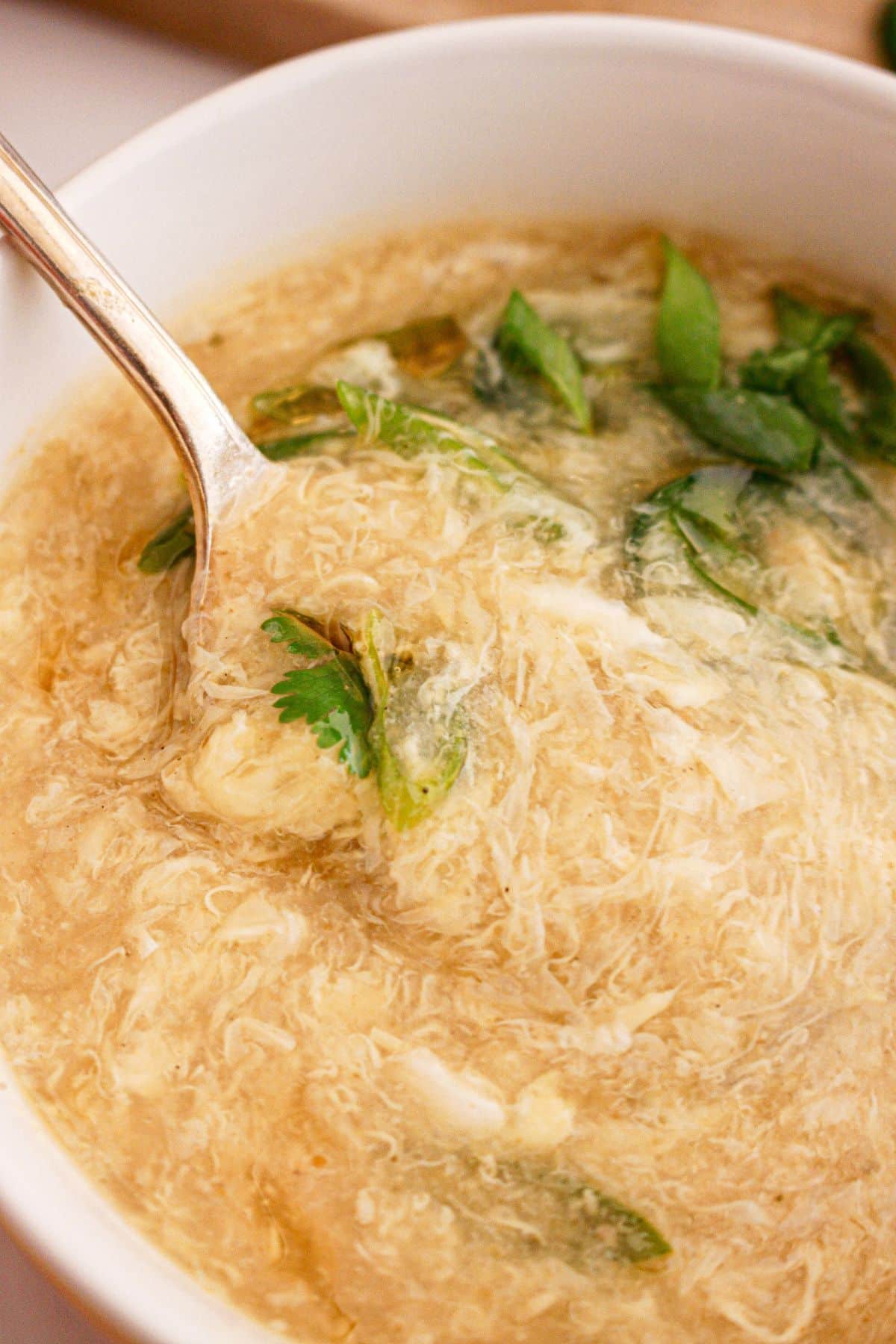 Bowl full of egg drop soup and garnished on cilantro and green onions.
