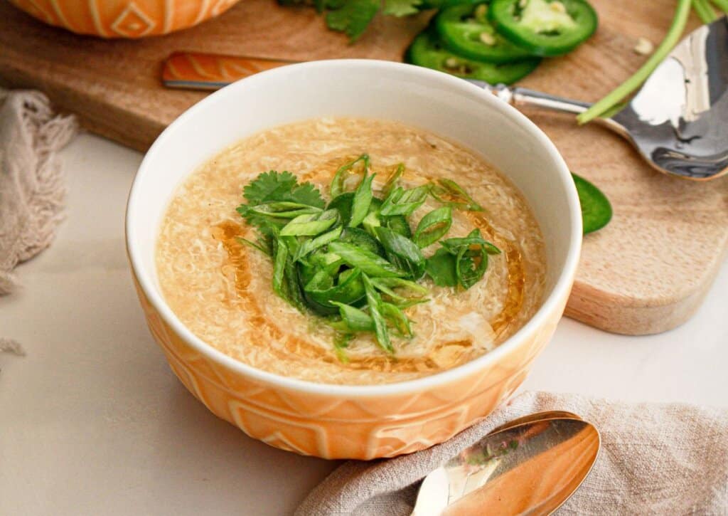 Bowl full of egg drop soup and garnished on cilantro and green onions.