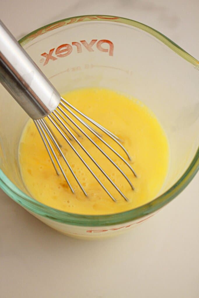 Eggs being whisked in a small measuring cup.