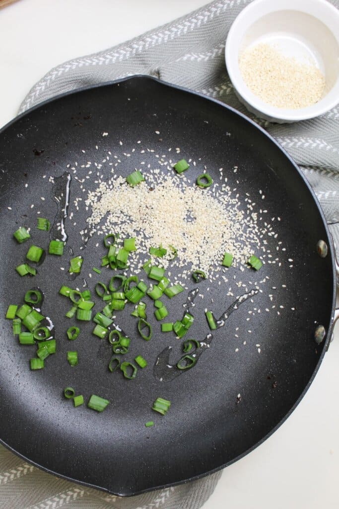 Green onions and sesame seeds in a skillet.