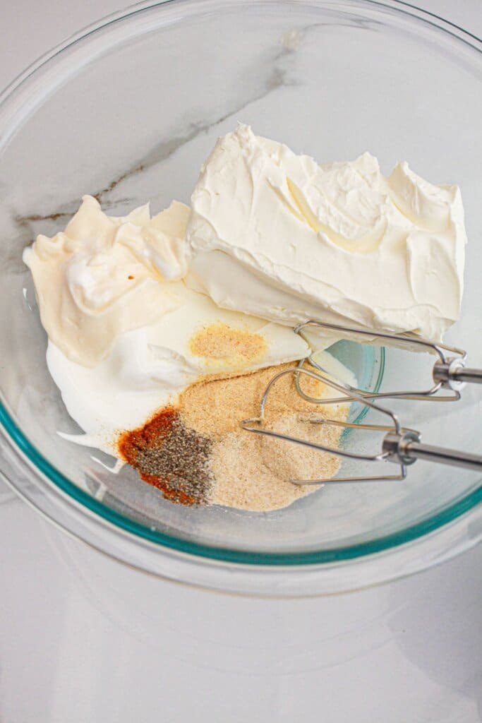 Cream cheese and seasonings being mixed in a glass bowl.