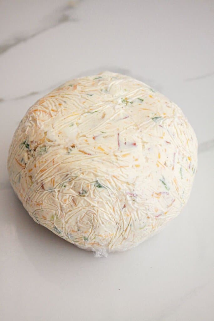 Cheese ball wrapped in plastic wrap on a counter.