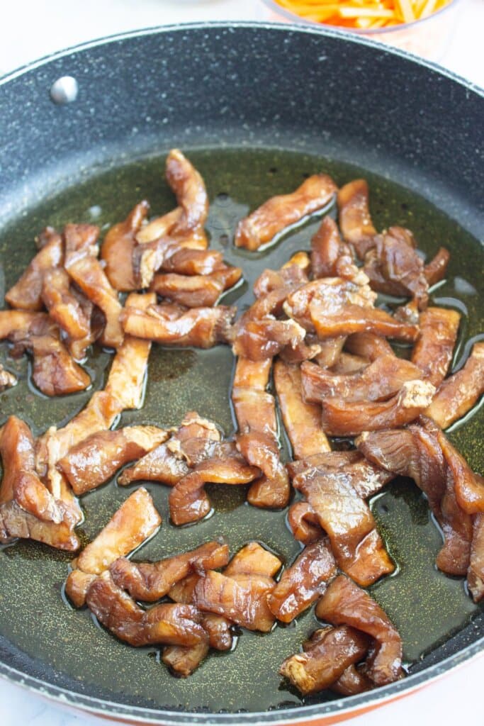 Pork tenderloin strips being cooked in a skillet.