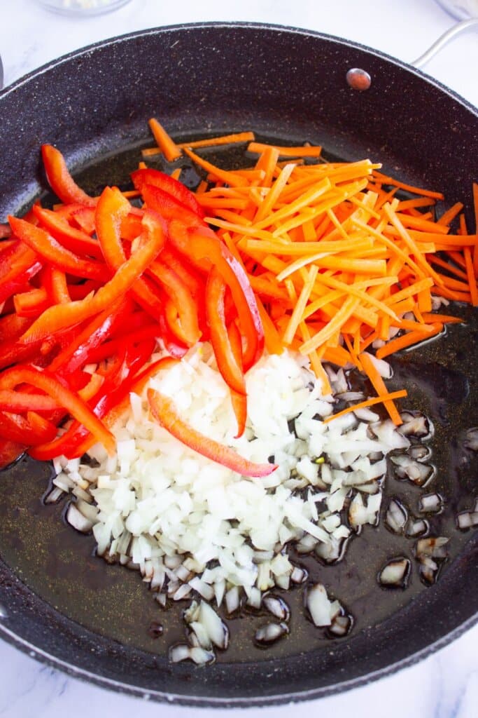 Carrots, onions, and bell peppers in a skillet.