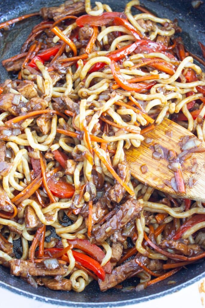 Carrots, onions, and bell peppers in a skillet with noodles.