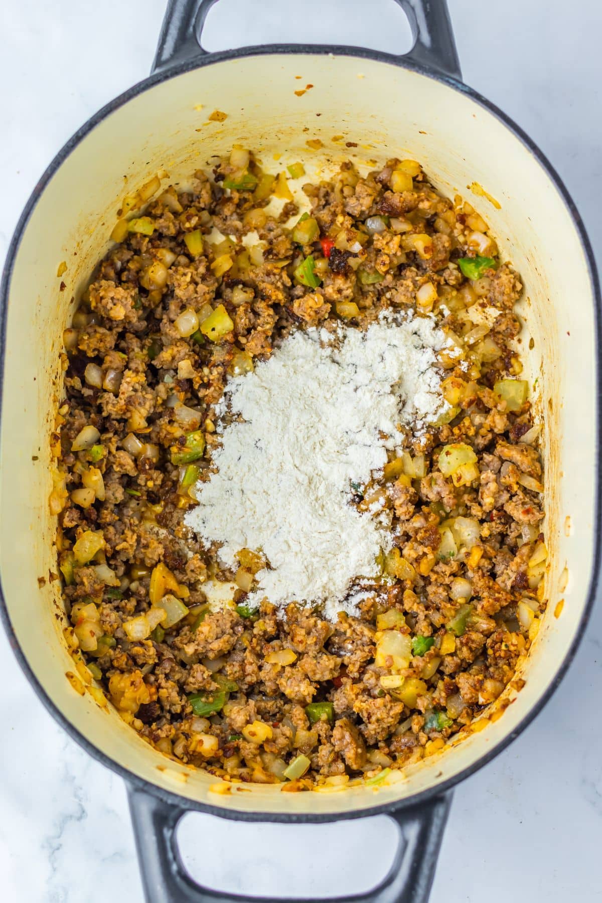 Flour being added to meat and veggies in a pot.
