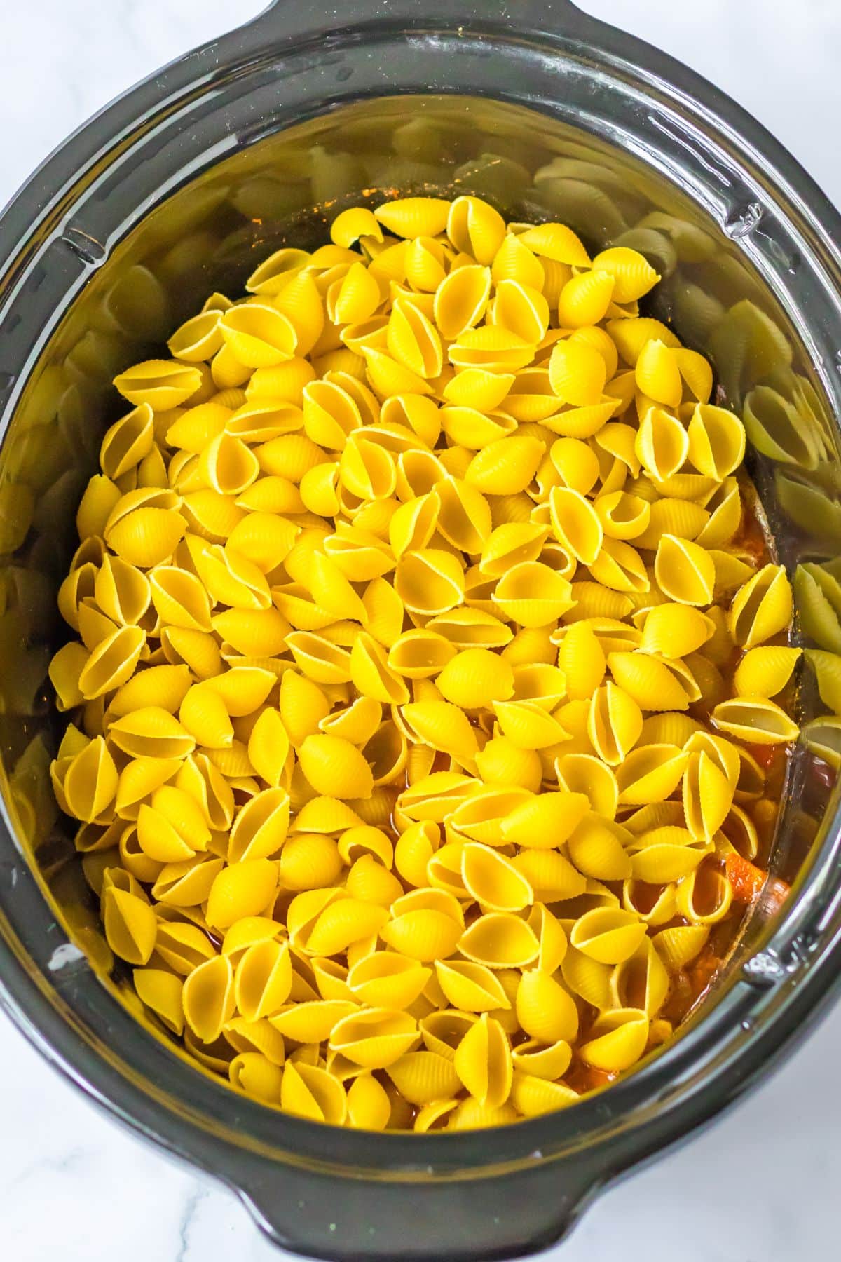 Dry noodles being added to crock pot.