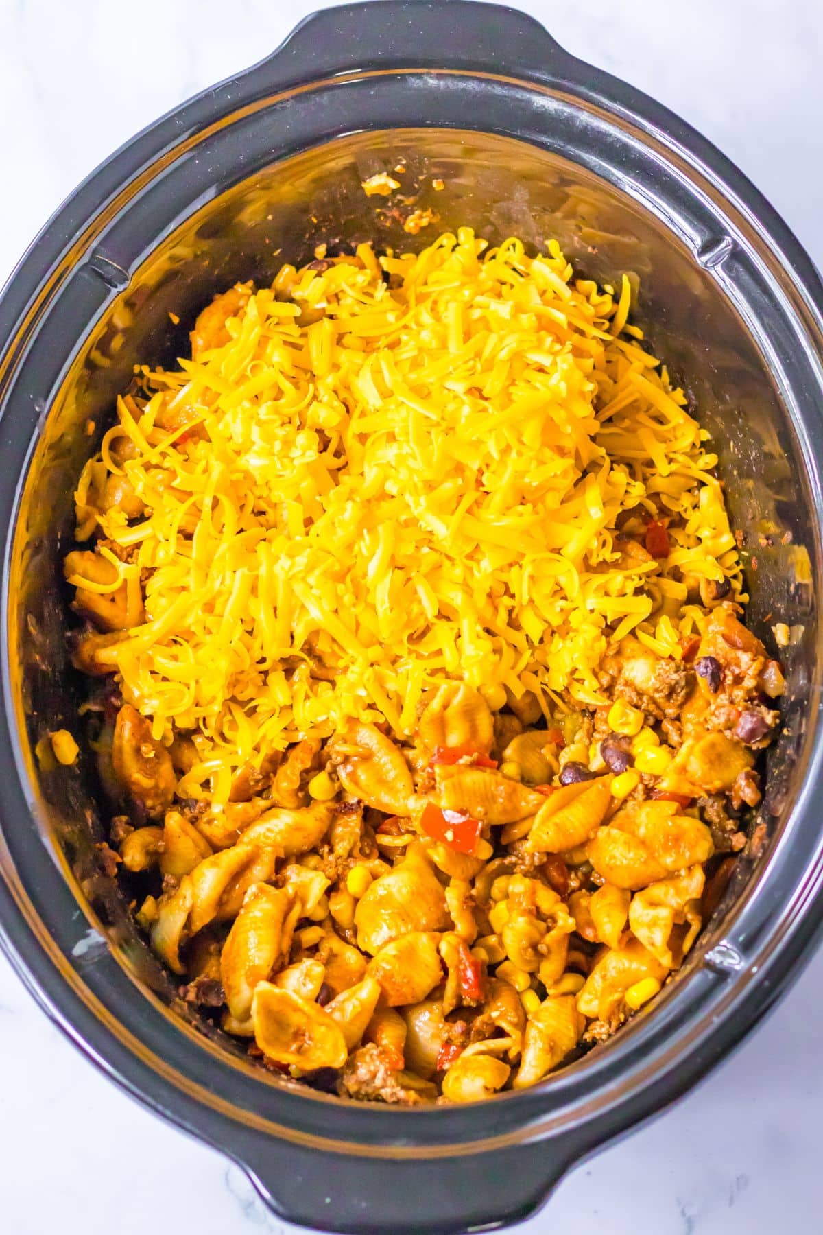 Cheddar cheese being sprinkled into crock pot.