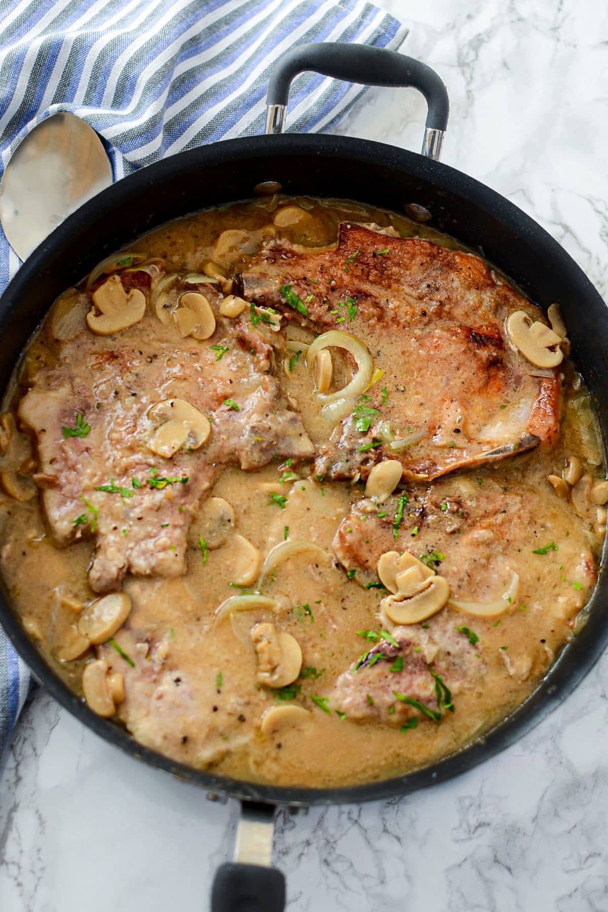 Smothered pork chops with mushrooms in a skillet.