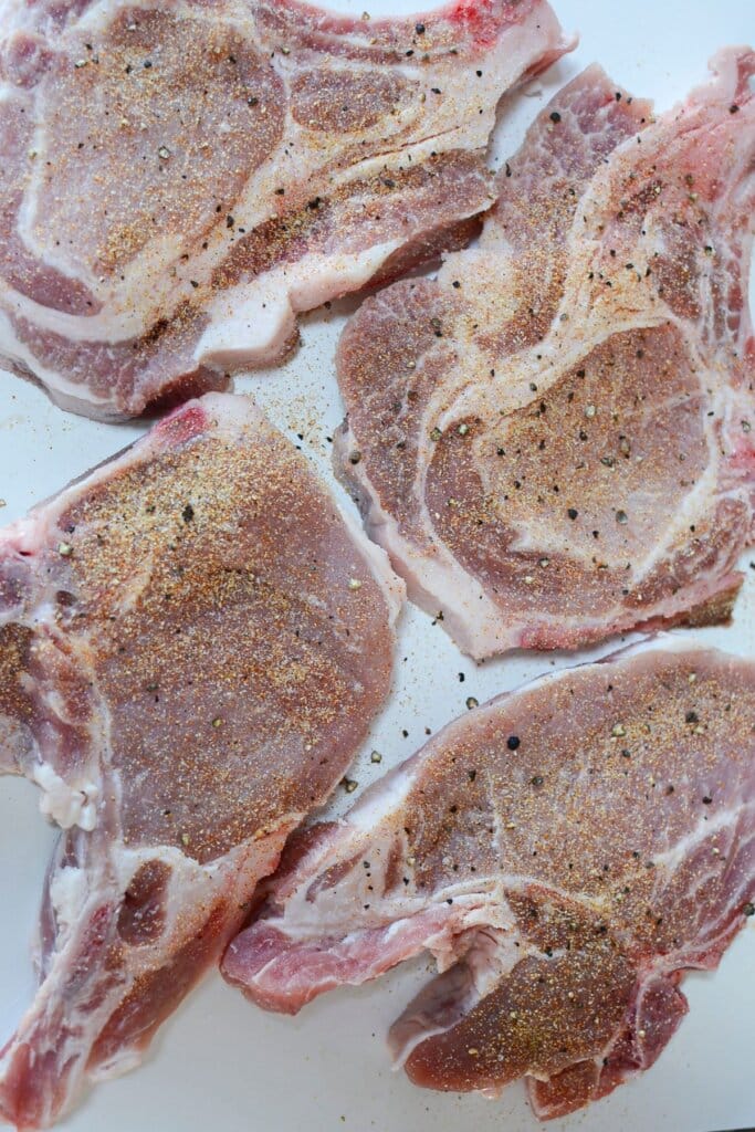 Pork chops being seasoned.