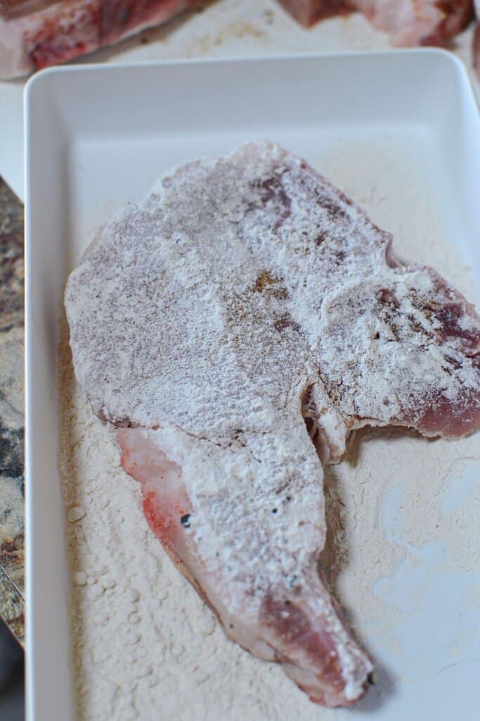 Pork chop being dredged in flour.