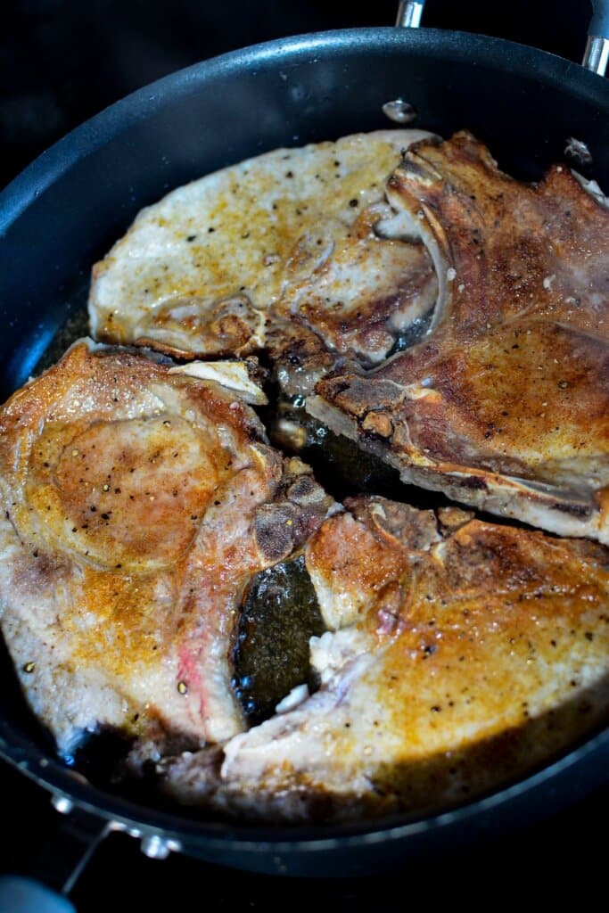 Pork chops being seared in a skillet.