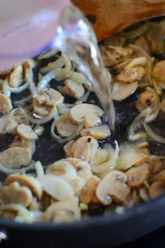 Water being added to a skillet with vegetables.