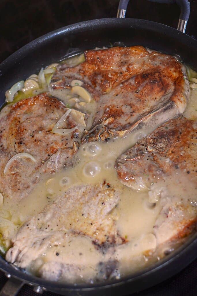 Pork chops and mushrooms in a skillet.