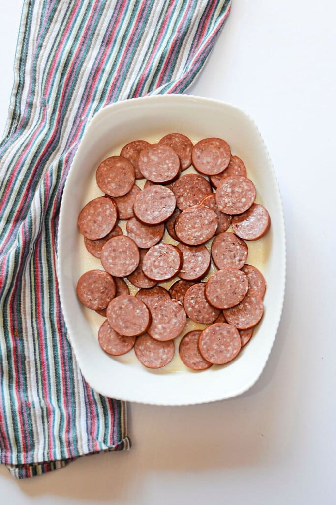 Smoked sausage being layered in a baking dish.