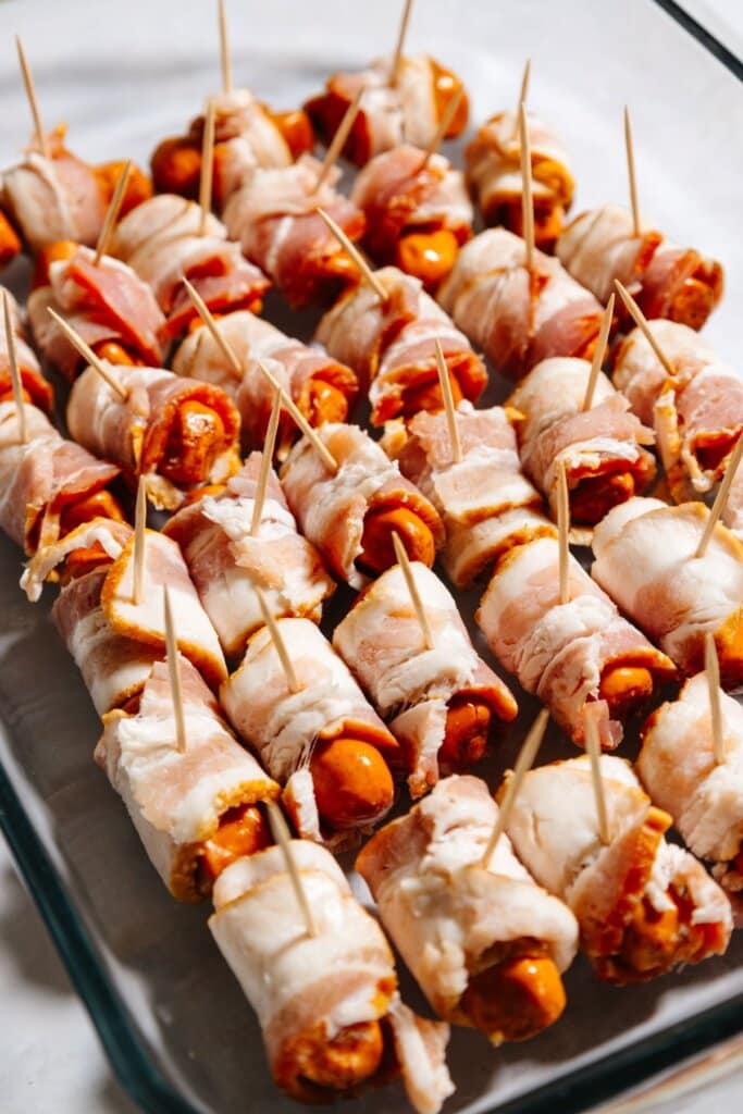 Uncooked baocn wrapped hot dogs in a glass baking dish.