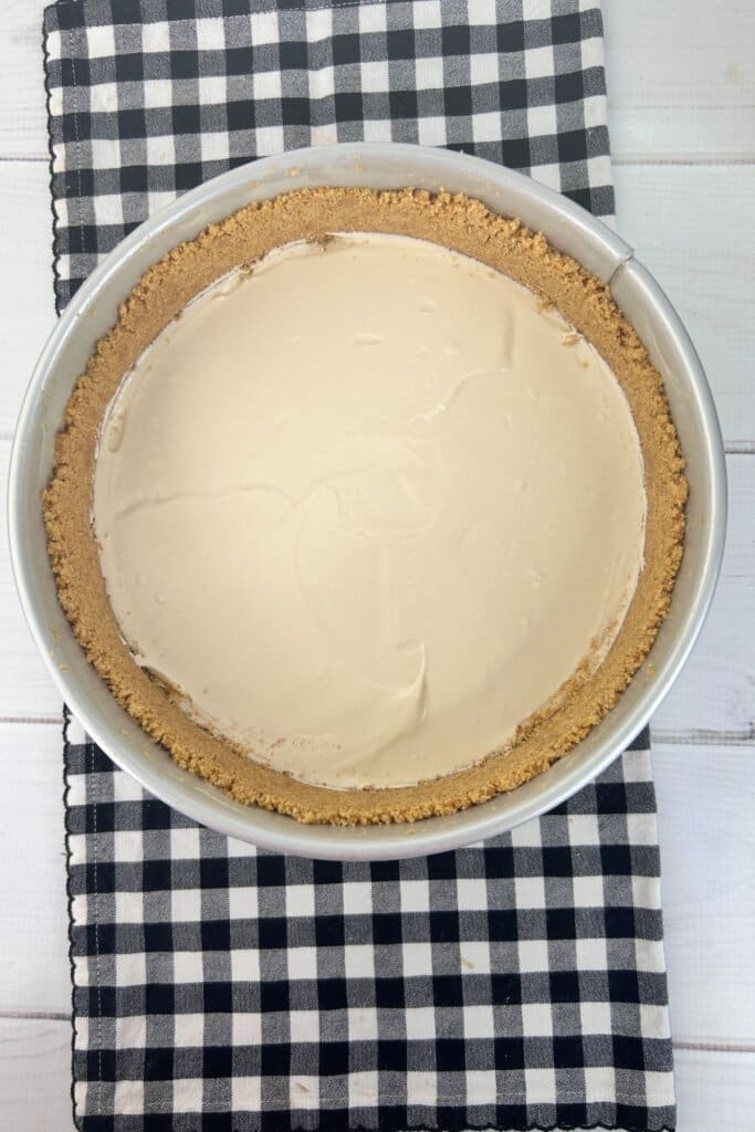 Batter being spread on top of crust in a springform pan.
