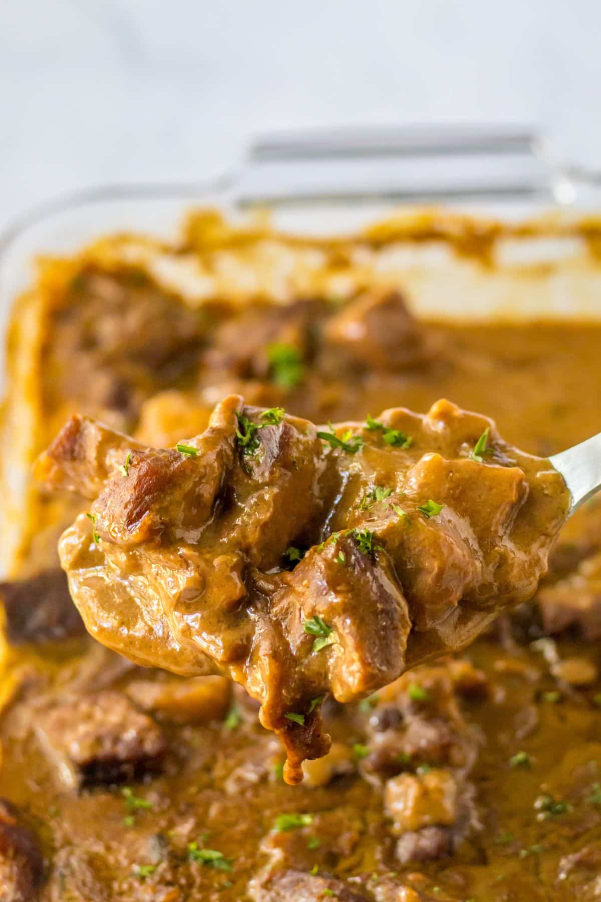 Serving spoon of beef tips and gravy held in the air.