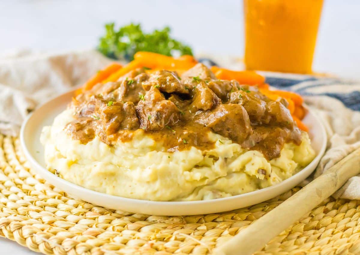 Beef tips on a plate on top of a bed of mashed potatoes.