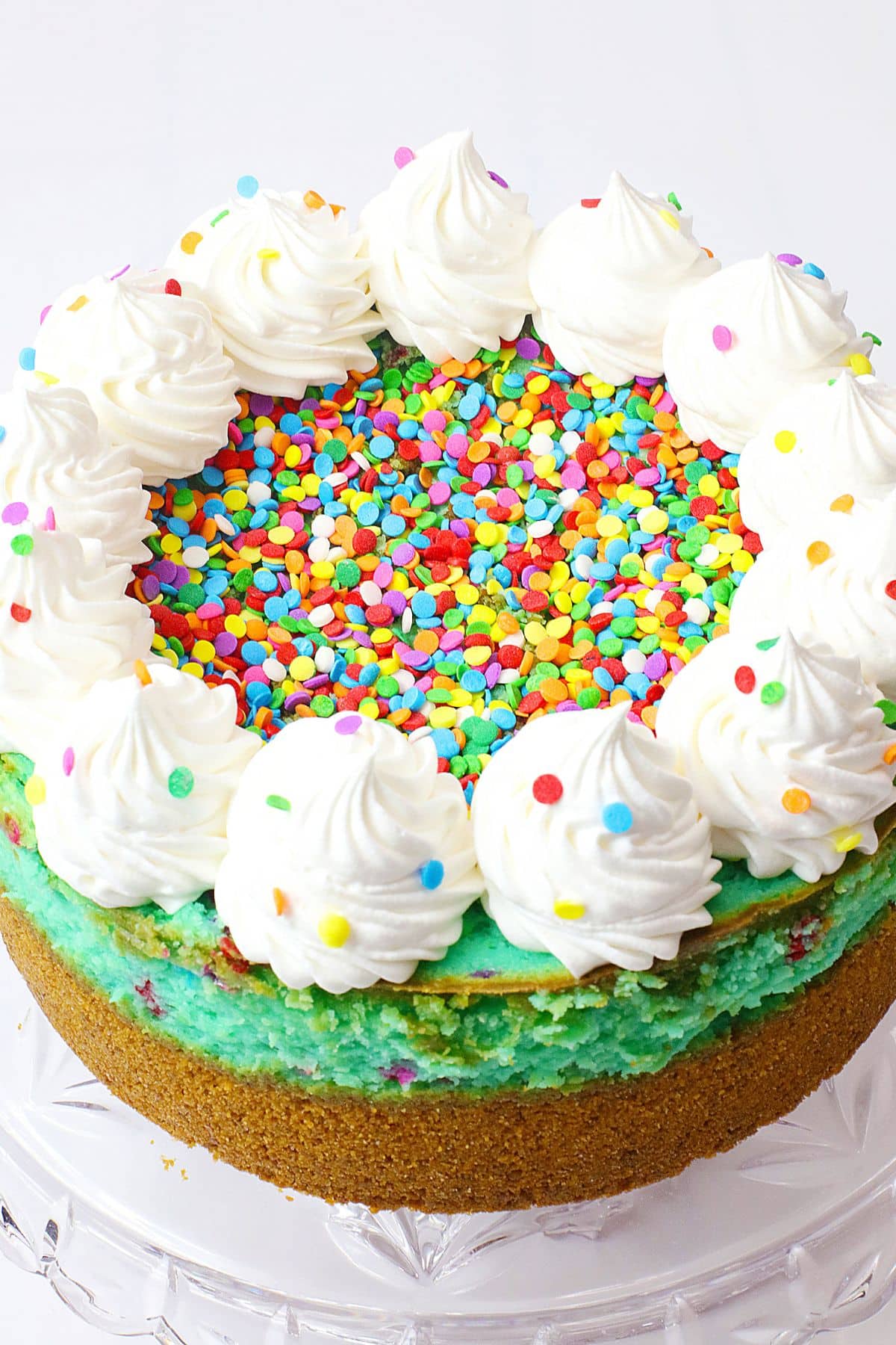 Birthday cake cheesecake on a glass cake stand.
