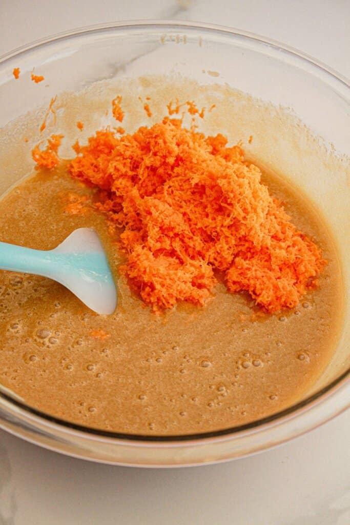 Carrots being added to batter in a glass mixing bowl.