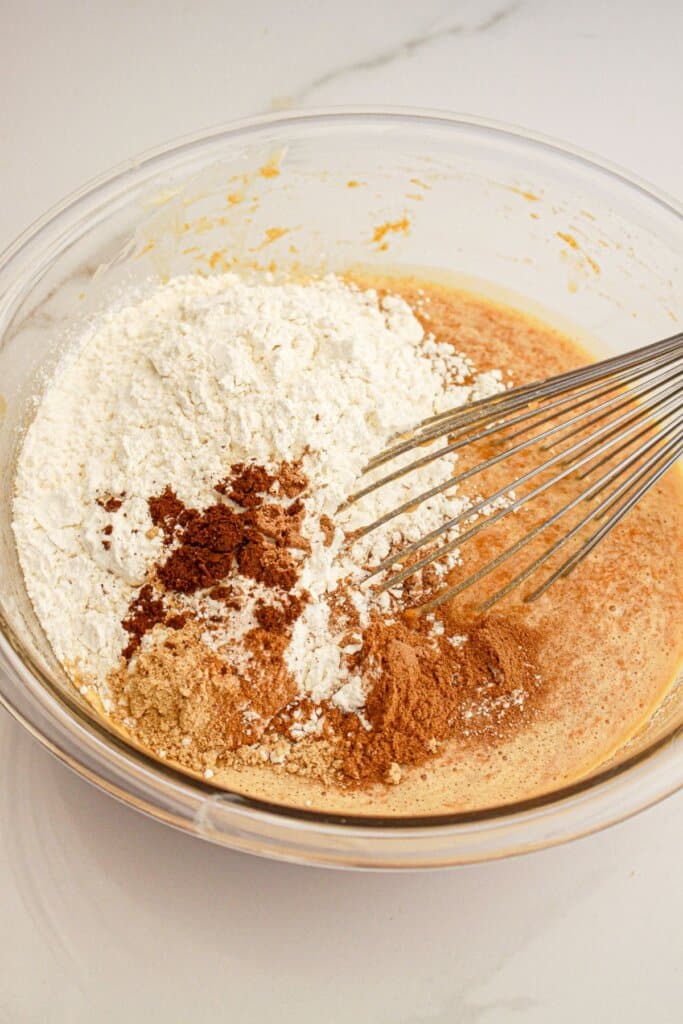 Dry ingredients being added to batter in a glass mixing bowl.