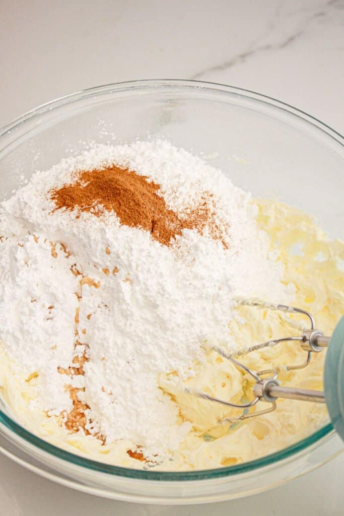Powdered sugar being added to butter in a mixing bowl.